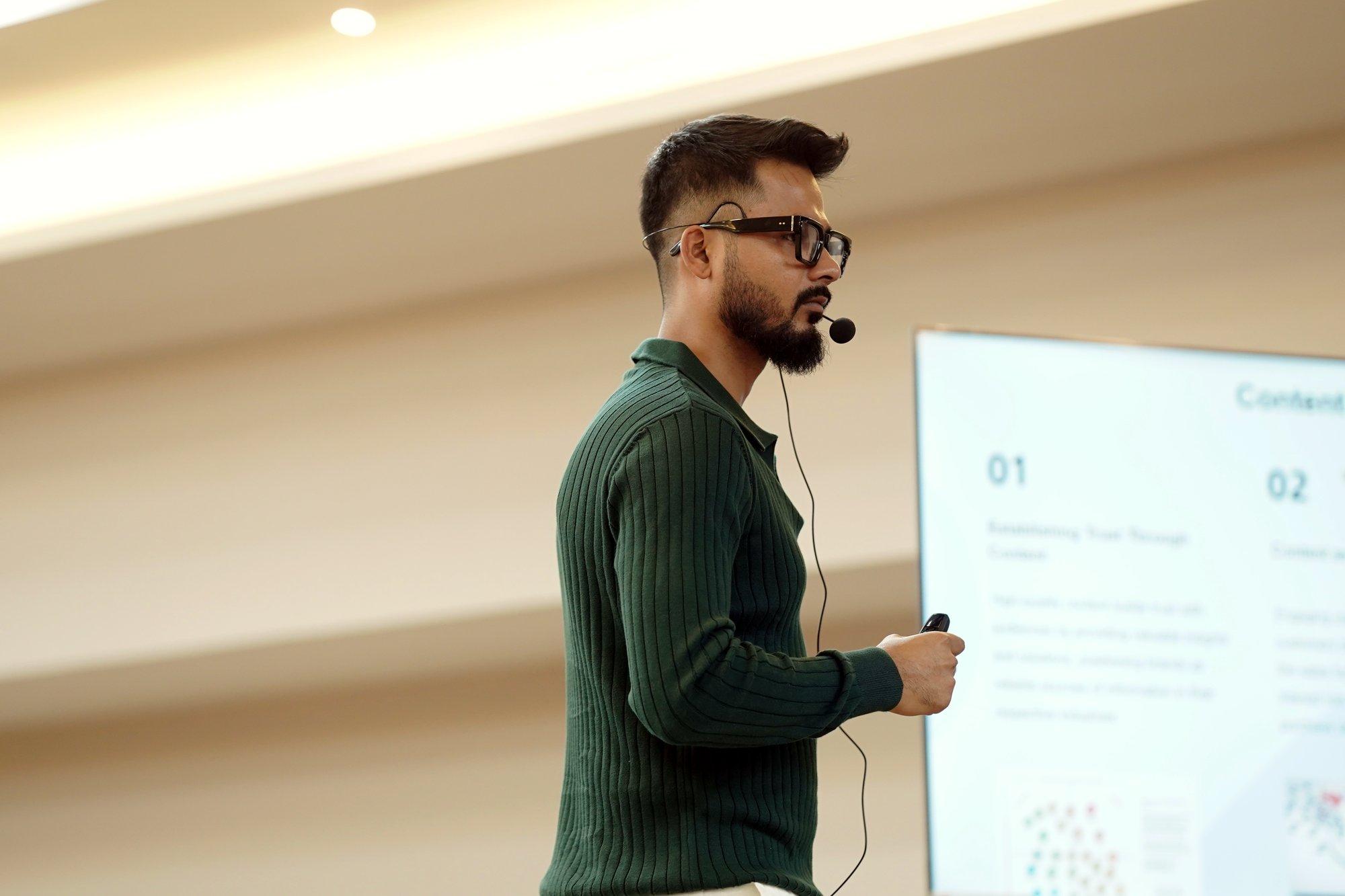 Roni Paul presenting with a headset mic, slides on screen behind him